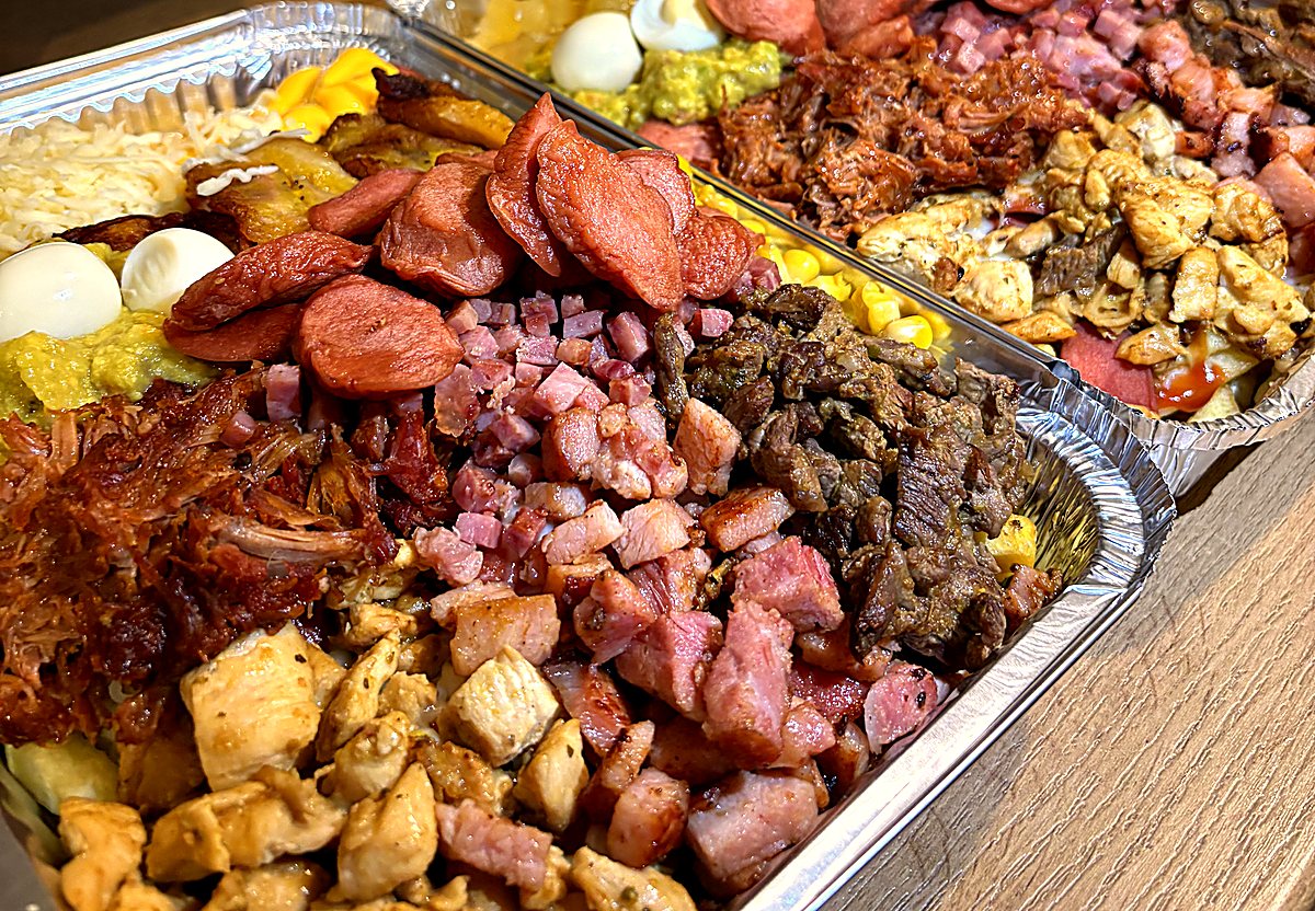Salchicausa cargada con los 13 toppings: carne, pollo, pulled pork, bacon, chuleta de sajonia, salchicha, huevo de codorniz, guacamole, cheddar, mozzarella, maíz, tajadas y piña